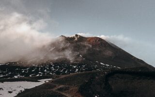 Foto di Asa Rogerche mostra Etna, semi avvolta da fumo e nuvole, colorata dalle vecchie colate laviche - foto utilizzata da geo etna explorer tour guidati privati e di gruppo sull'Etna escursioni in jeep