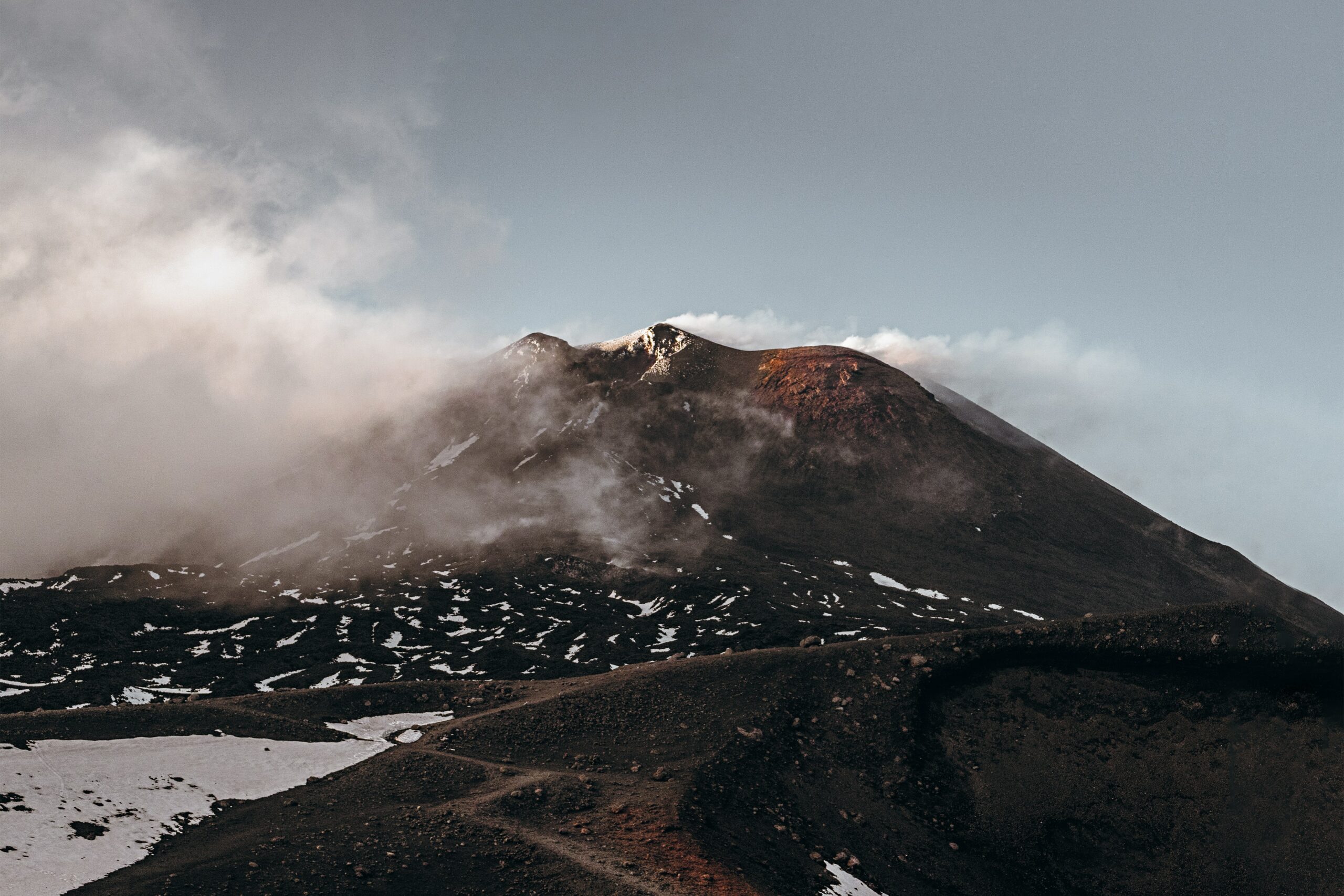 Foto di Asa Rogerche mostra Etna, semi avvolta da fumo e nuvole, colorata dalle vecchie colate laviche - foto utilizzata da geo etna explorer tour guidati privati e di gruppo sull'Etna escursioni in jeep